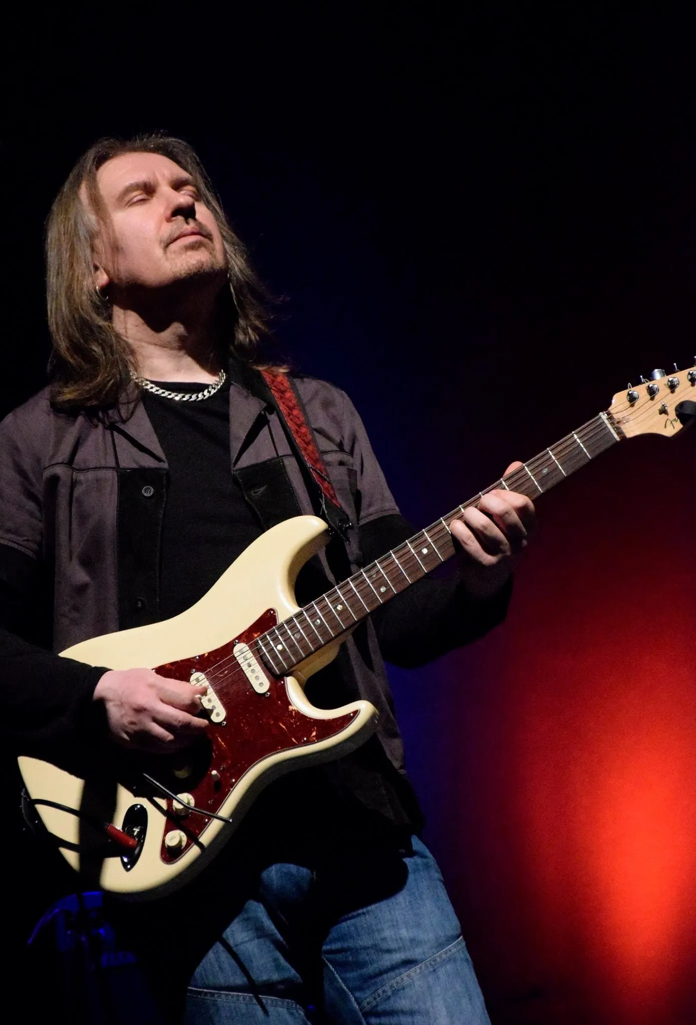 Misha Nikolic performing live with a cream Strat-style guitar.