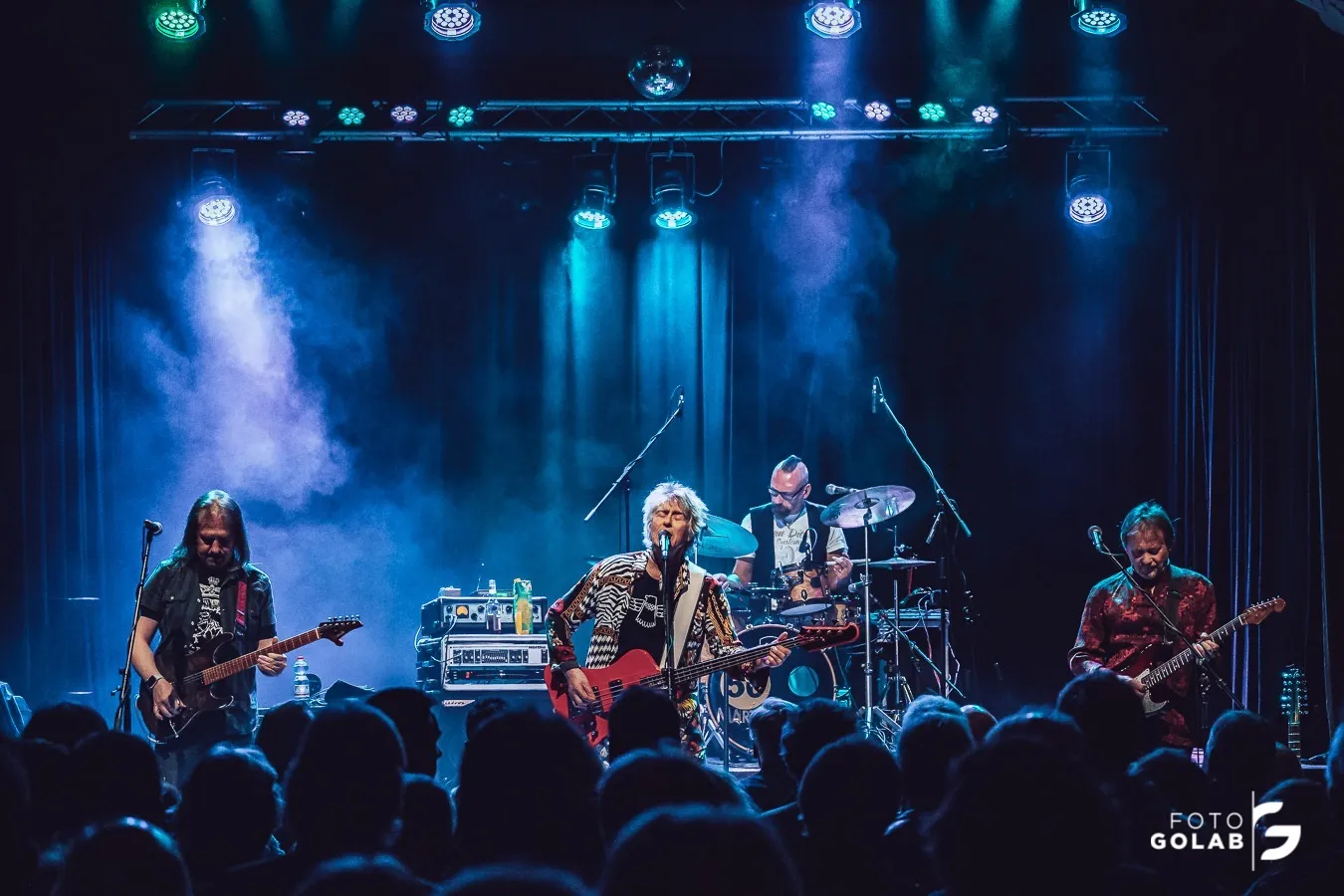 Misha Nikolic performing live on stage in a wide band performance shot.