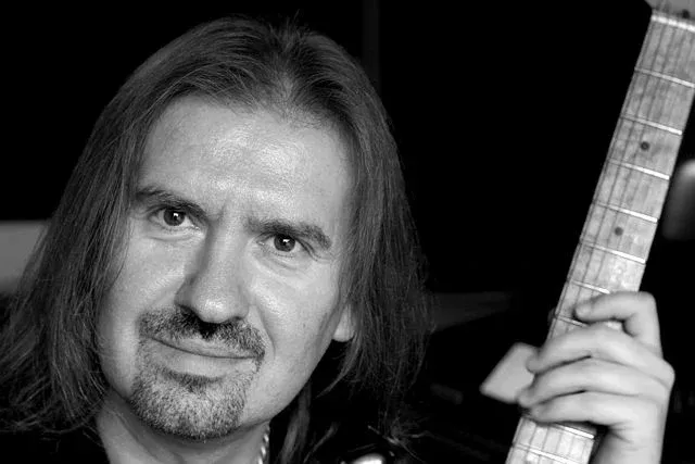 Black and white portrait of Misha Nikolic holding a guitar.